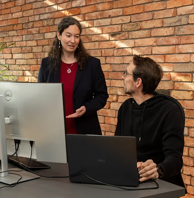 Eine Mitarbeiterin und ein Mitarbeiter der codemanufaktur unterhalten sich vor ihrem Laptop.