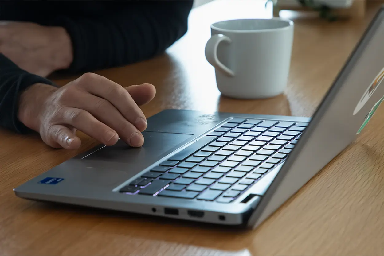 Eine Nahaufnahme von einem Kollegen, der das Touchpad seines Laptopds bedient